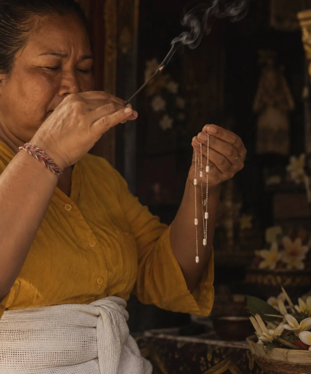 Balinese healer holding a pearl necklace during a metta ritual with incense